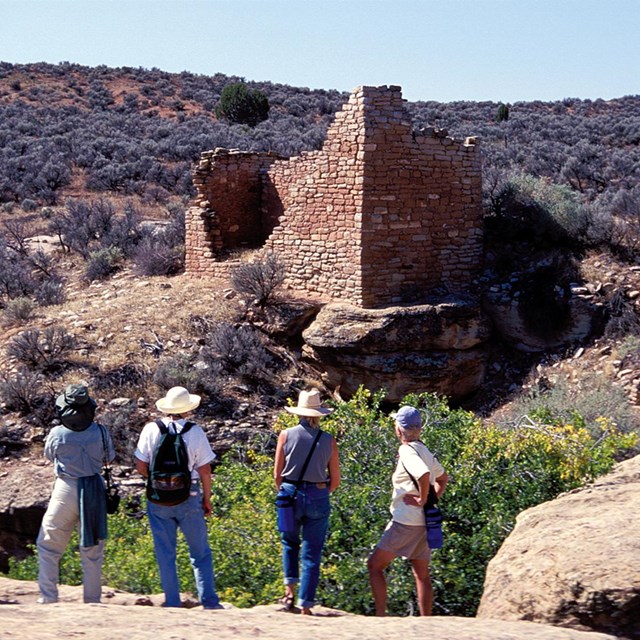 People on a canyon rim overlooking a large stone structure