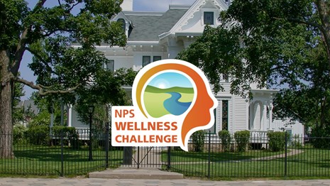 Modern photo of Truman Home, white house, metal fence in front, round logo for wellness challenge.