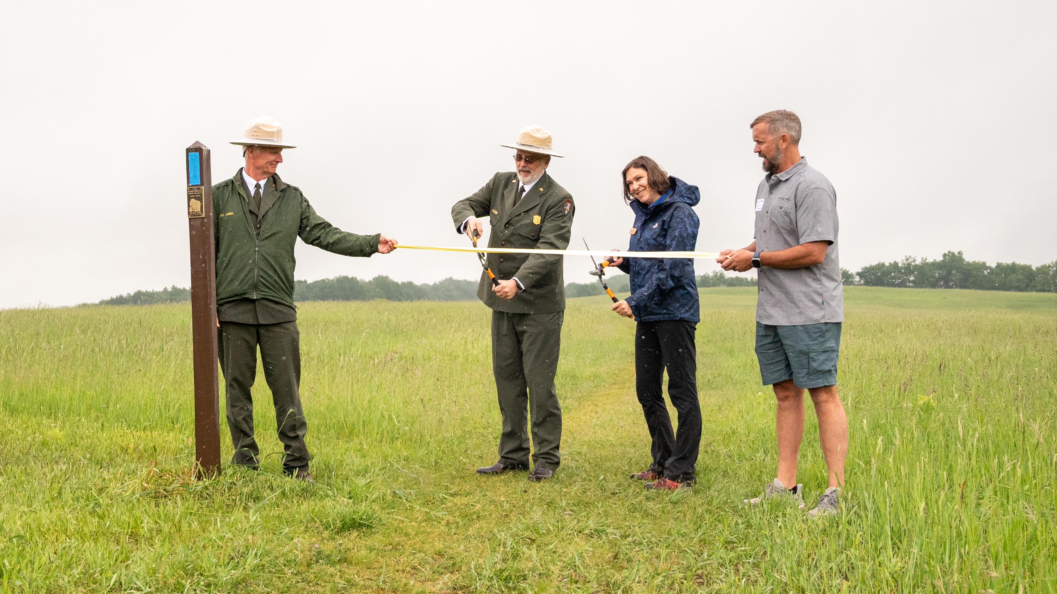 Photograph of four people cutting a ribbon in a green field. 