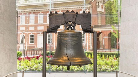 Color photo showing the Liberty Bell in the foreground with Independence Hall visible behind.