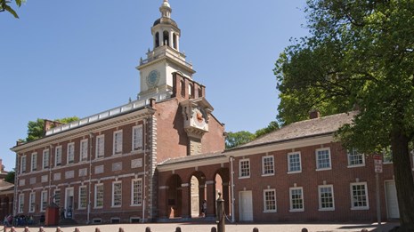 Color photo of Independence Hall, a two story red brick building with many windows and clock tower.