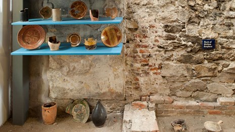 Color photo showing an exhibit with pottery and shards on shelves and on a dirt floor.
