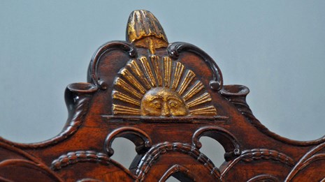 Color photo showing a detail from a chair's crest rail with a carved sun and liberty pole and cap.