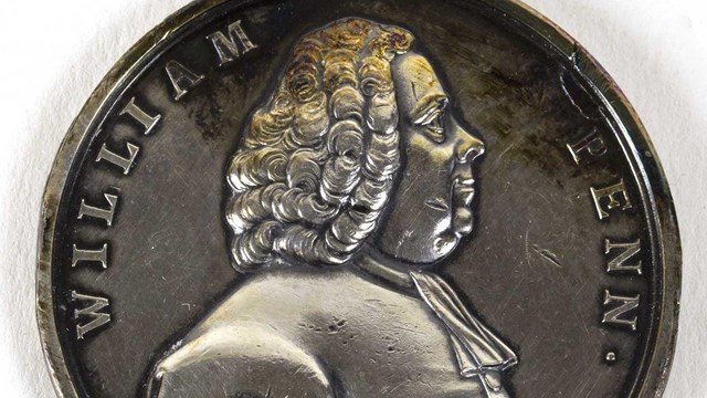 silver coin with bust of man with curly wig