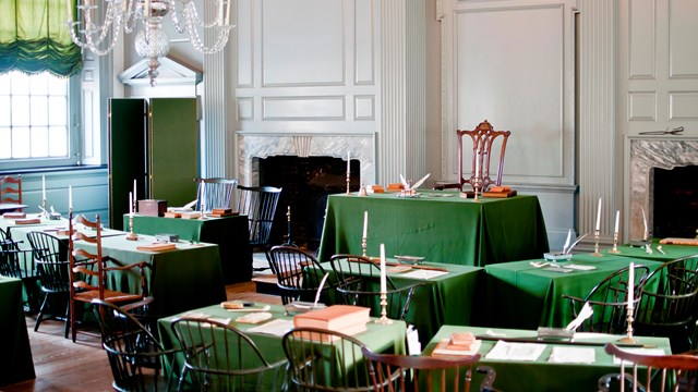 Color photo of the Assembly Room with rows of tables covered with green cloth facing a head table.