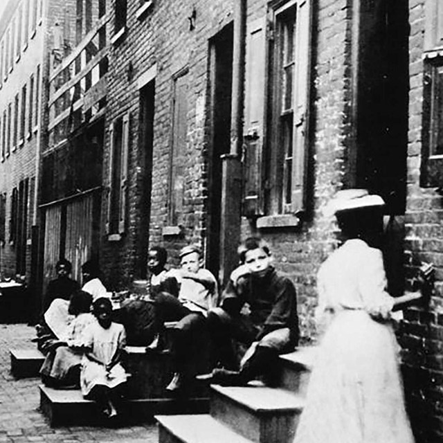 black and white image of children and an adult outside of homes on stoops