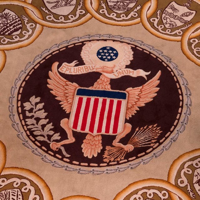 Color photo showing a detail from a carpet featuring the Great Seal of the U.S.