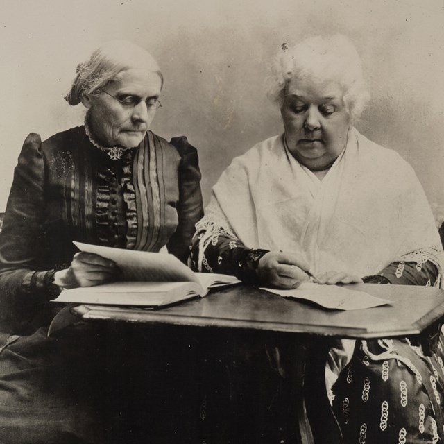 Black and white photo of two women from the late 1800s seated at a table.