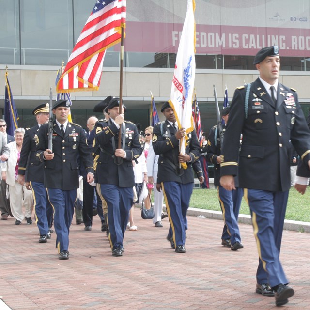 Color photo of men in military uniform marching near the National Constitution Center