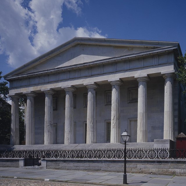 Color photo of a two-story marble building with several columns supporting a triangular pediment.