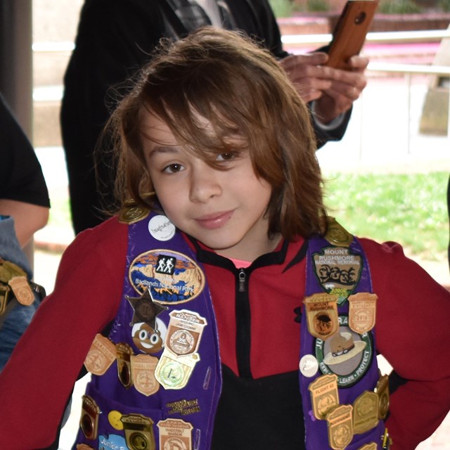 Young girl wearing a vest adorned with junior ranger badges.