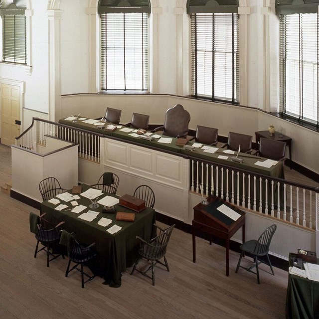Color photo looking down on courtroom, showing raised bench for judges with table below.