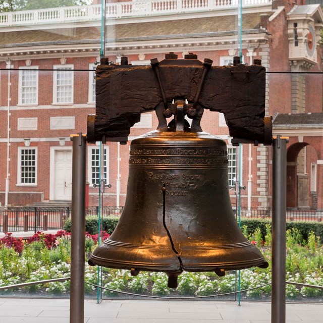 Color photo showing the Liberty Bell in the foreground with Independence Hall visible behind.