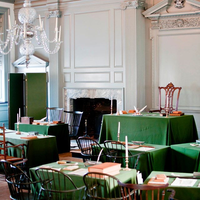 Color photo of Assembly Room with green cloth-covered tables facing a single table up front.