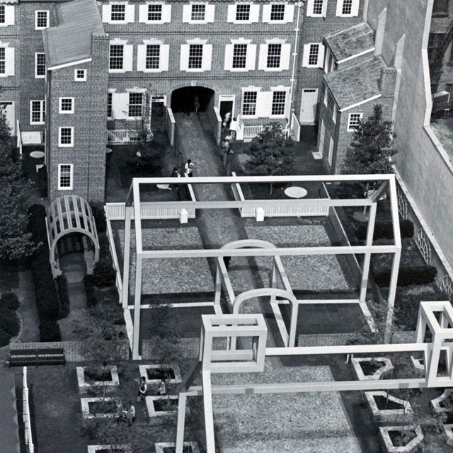 Black and white aerial view photo showing a courtyard with two steel frame house structures.