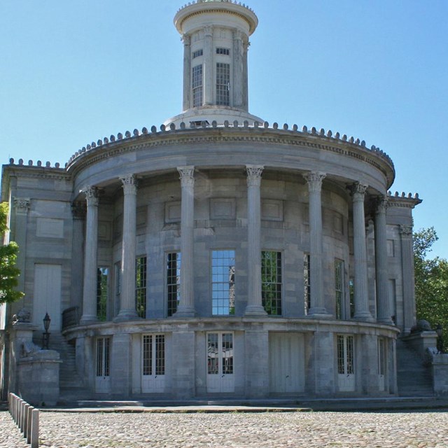 Color photo of two-story marble building with rounded facade and several columns.