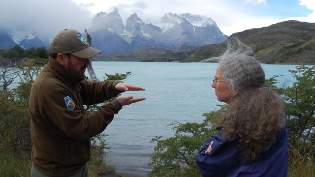 A National Park Service ranger talks with a Chilean park ranger in front of a lake.