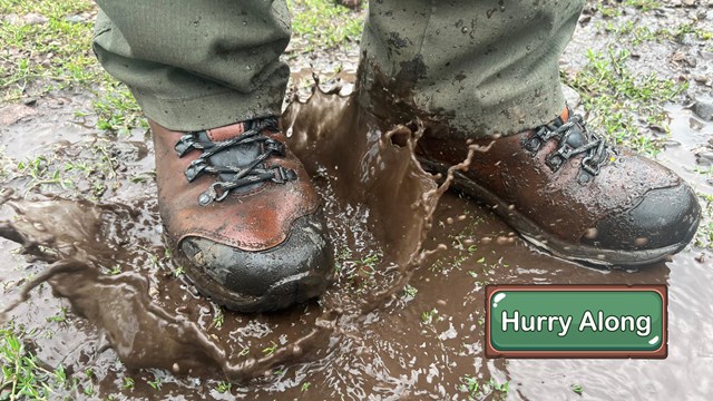 Close up of hiking boots splashing in a muddy puddle.