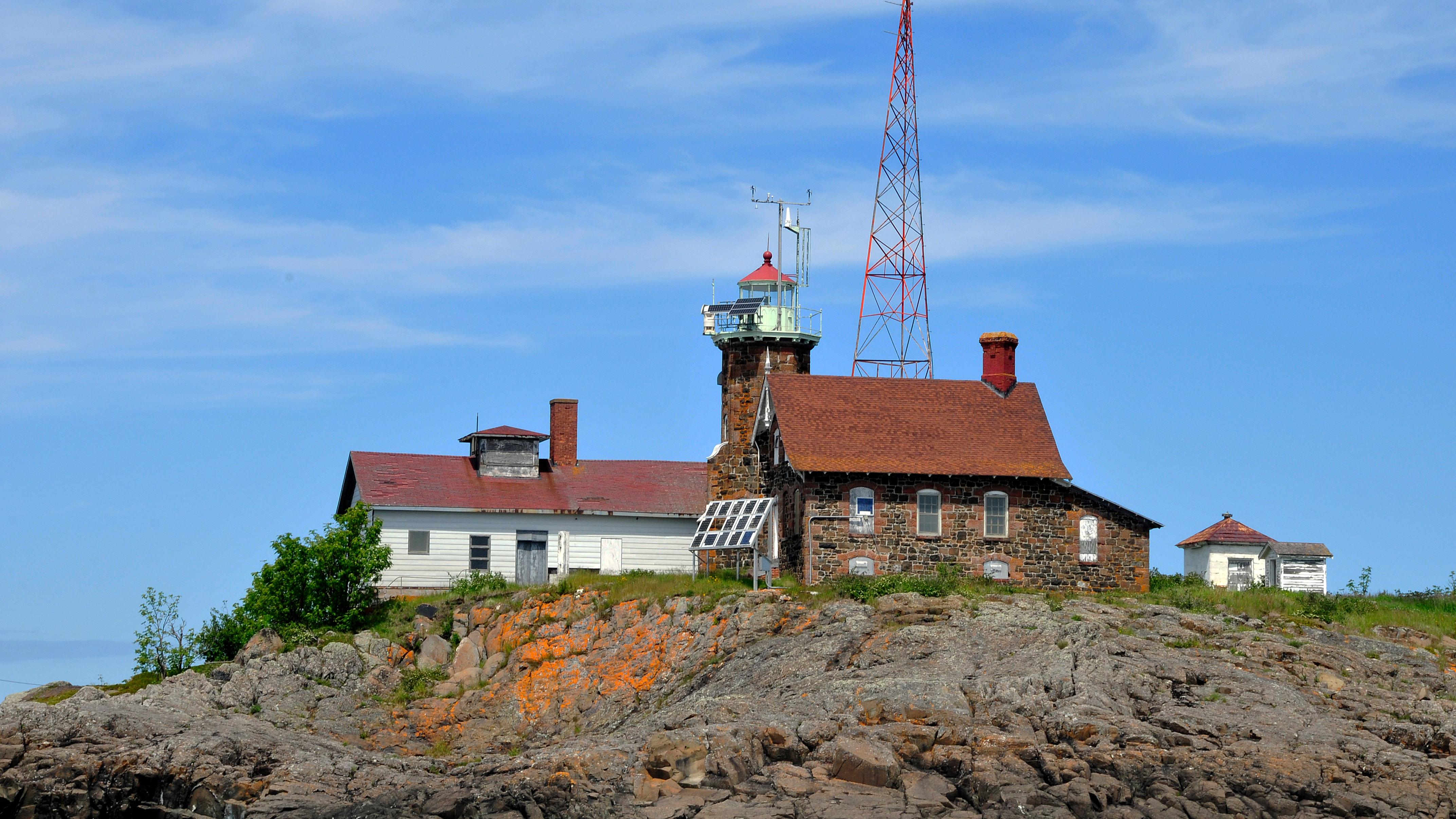 view of the rocky shoreline in the foreground of the Passage Island lighthouse, garage, and tower