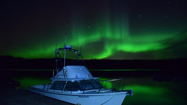 Green northern lights shine and reflect off the water on the Windigo dock.