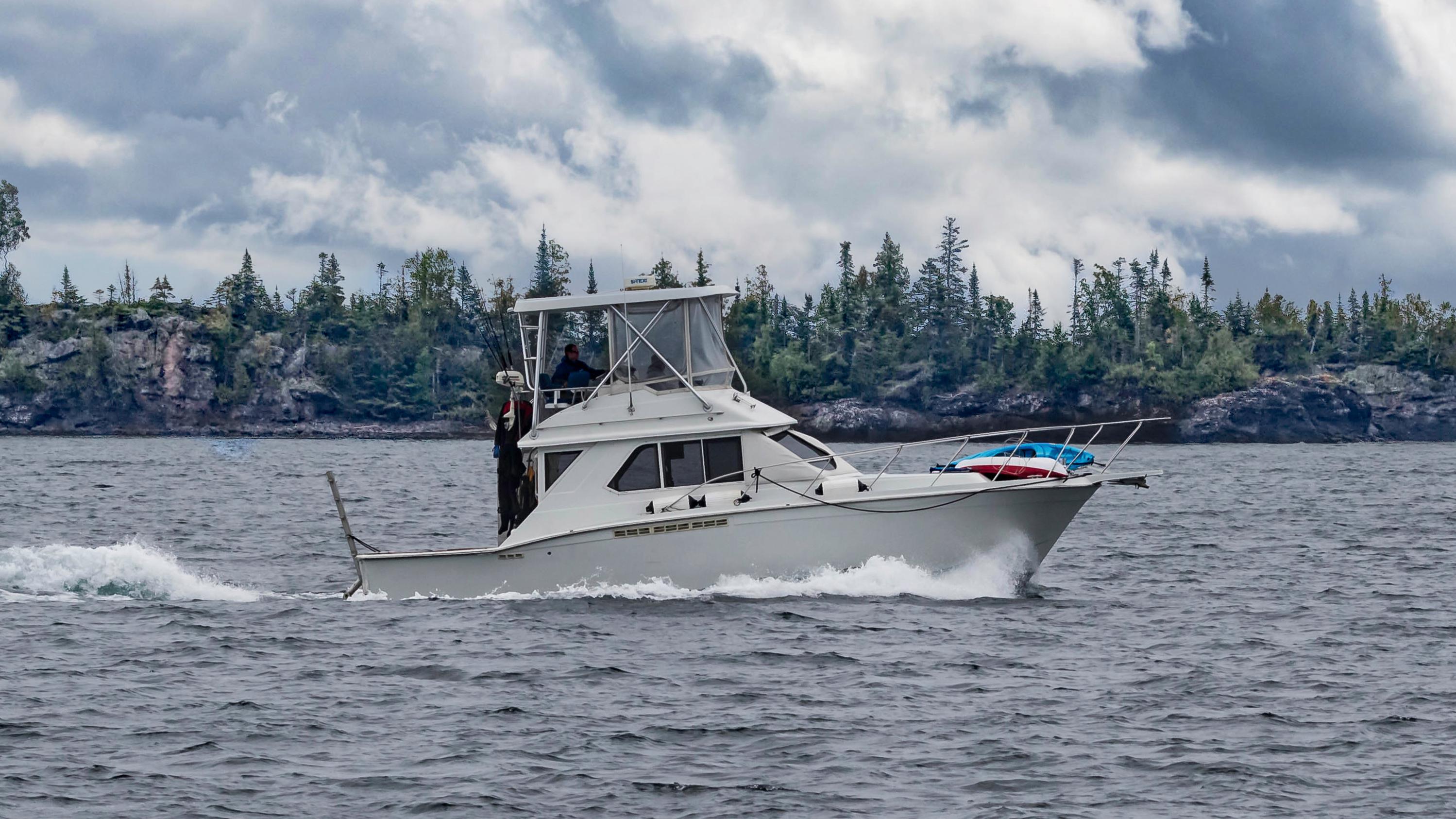 A white powerboat sailing in a lake near a rocky island.