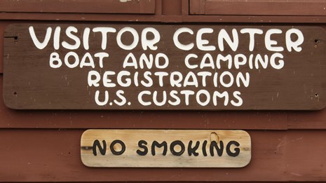 A wooden sign says "Visitor Center Boat and Camping Registration U.S. Customs"