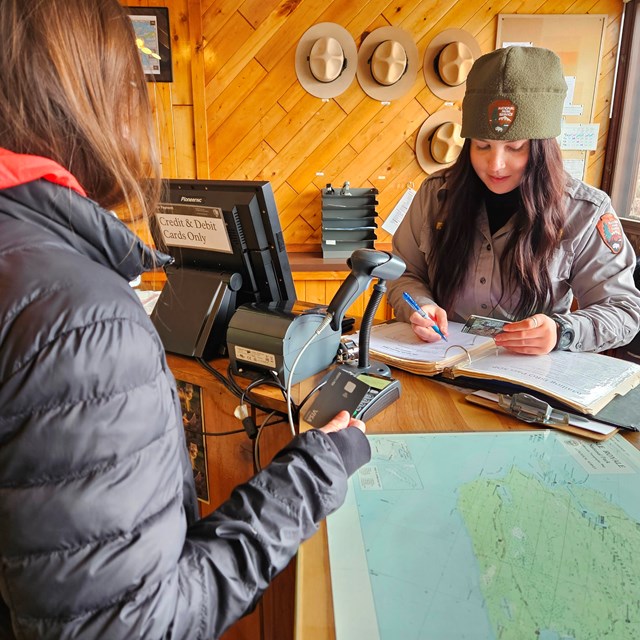 A park ranger at a desk selling a pass to a visitor. 