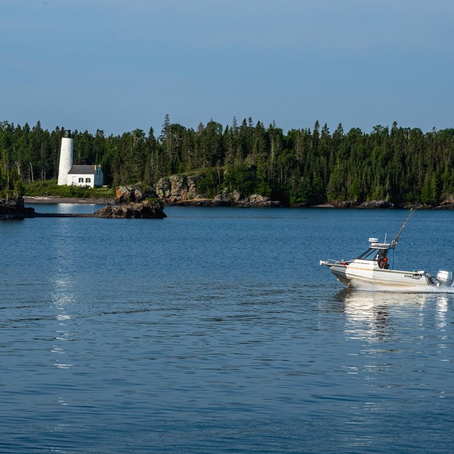 Powerboat boating in the rock harbor channel past the Rock Harbor lighthouse.