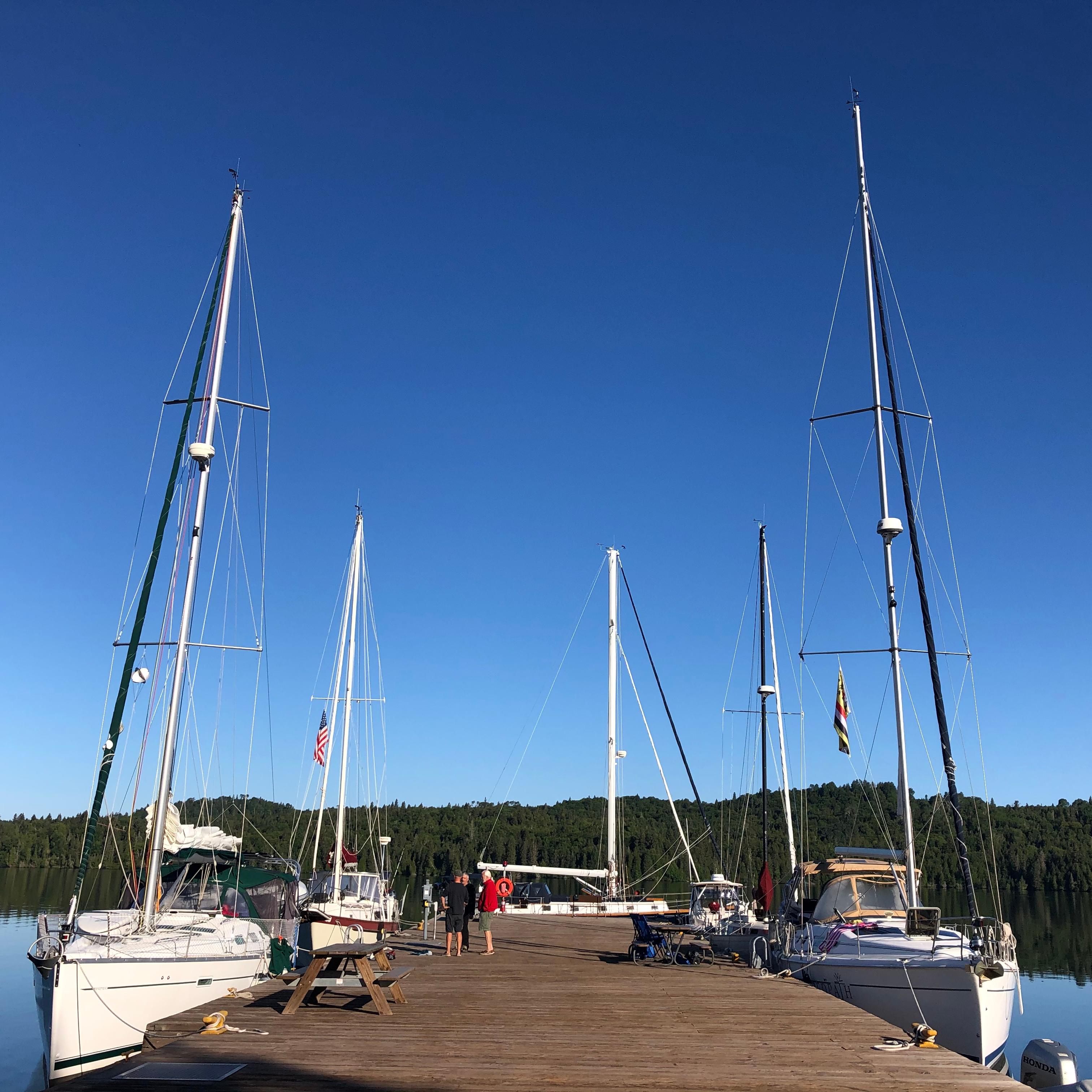 Multiple sailboats are docked around a large, wooden dock.
