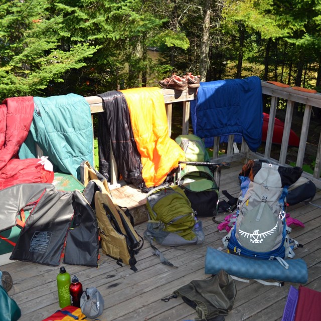 Backpacking gear spread out on a deck, life jacket, water bottles, clothing, tent supplies, etc.