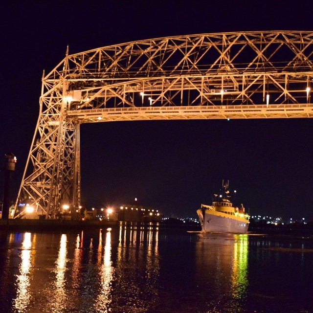Night photo of Ranger III passenger ferry traveling beneath lit-up Houghton Lift Bridge. 