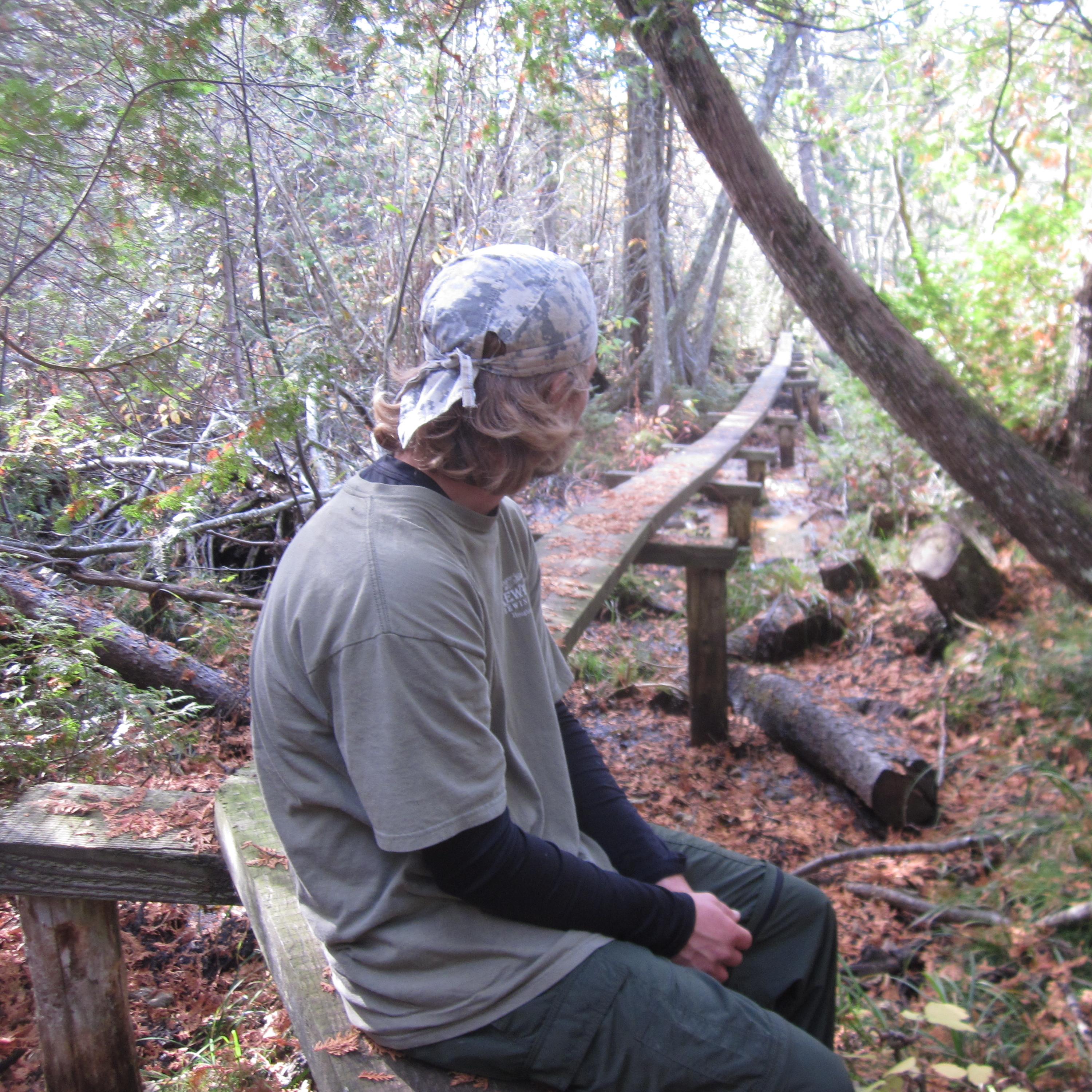 A person sits on a wooden plank bridge surrounded by trees on Isle Royale. 