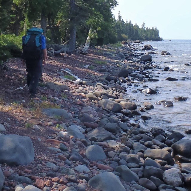 A backpacker hiking along the rocky Lake Superior shoreline.