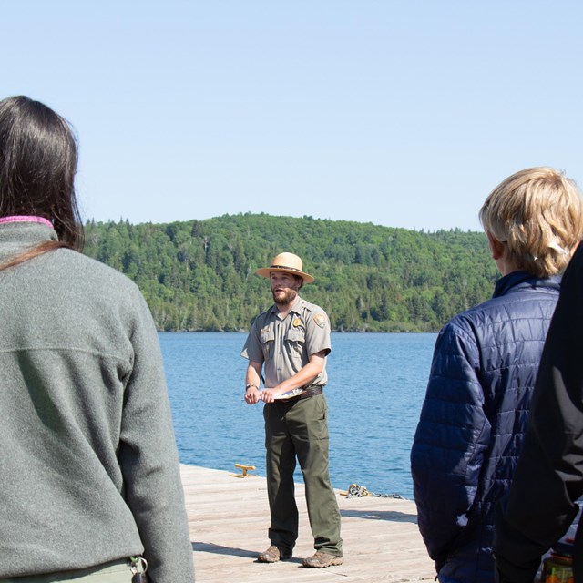 A Park Ranger with a clipboard talking with visitors on a dock. 