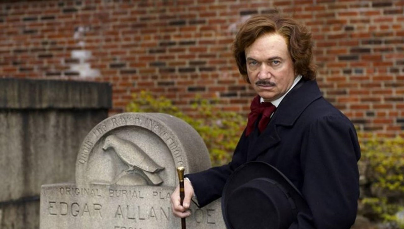 Man dressed as Poe standing next to Poe's headstone.
