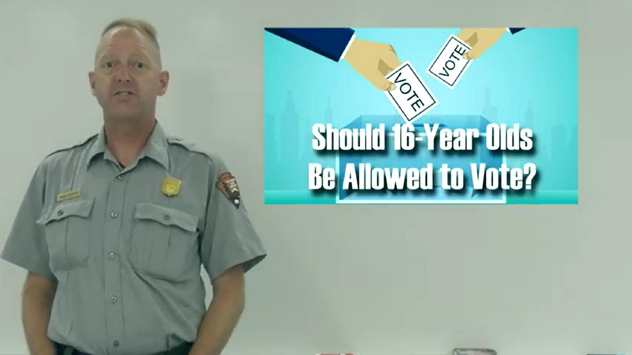 A park ranger stands next to a graphic that says "should 16-year-olds have the right to vote"