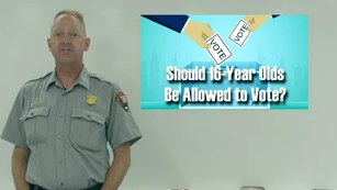 A park ranger stands next to a graphic that says "should 16-year-olds have the right to vote"