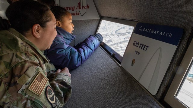 A woman and a child look out of a window on the observation deck at the top of the Gateway Arch.