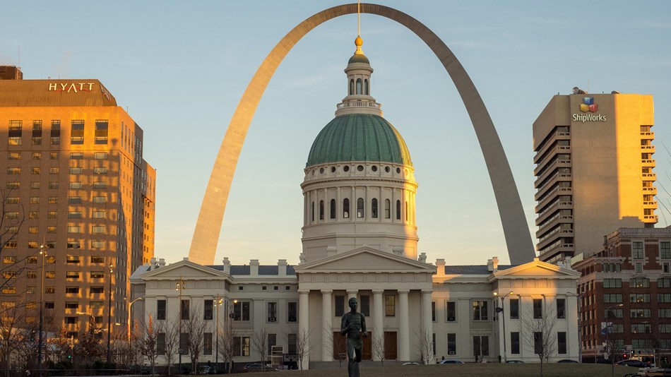 Image of 630 foot steel arch with green and white stone courthouse in forefront.