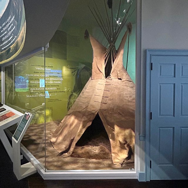 A cone-shaped tipi behind glass in a museum
