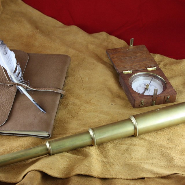 Leather-bound journal with feather, compass in a square wooden case, refracting telescope