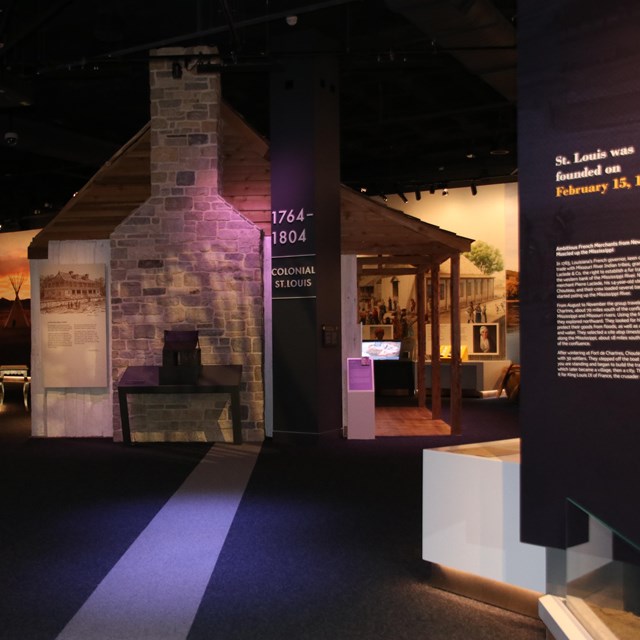 A dark museum gallery with a replica creole cabin centered in the image