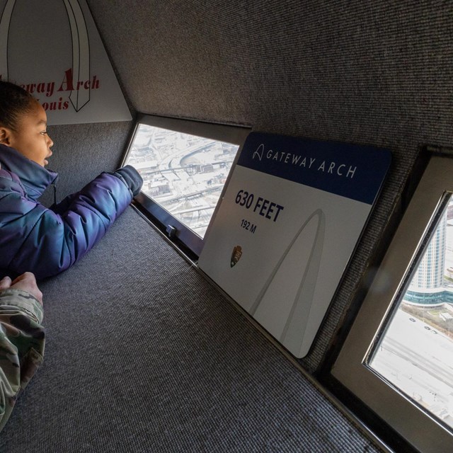 A woman and a child look out of a window on the observation deck at the top of the Gateway Arch.