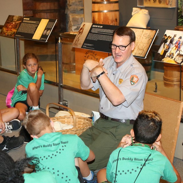 Park Ranger sitting with children and leading a program in front of a museum exhibit. 