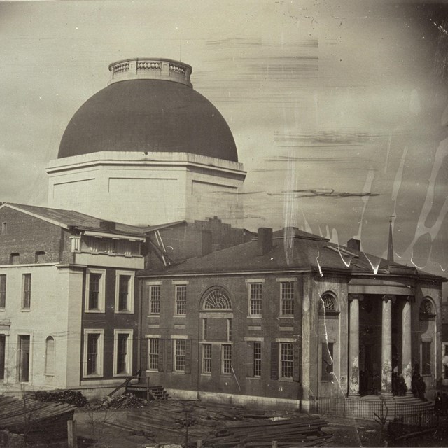 Black and white photo of rectangular stone courthouse with round copper roof.