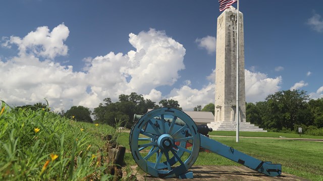 A cannon faces the battlefield in front of the Chalmette Monument and an American flag
