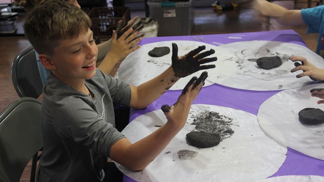 A boy looks at his hands covered in dark mud and smiles.