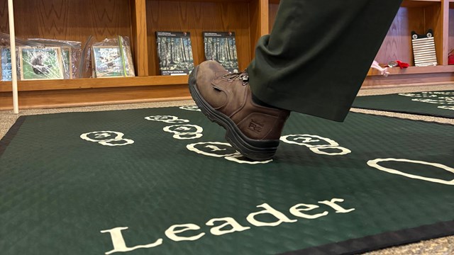A park ranger touches a nutria fur with a kid at a table.
