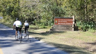 Bicyclists ride by the Barataria Preserve sign