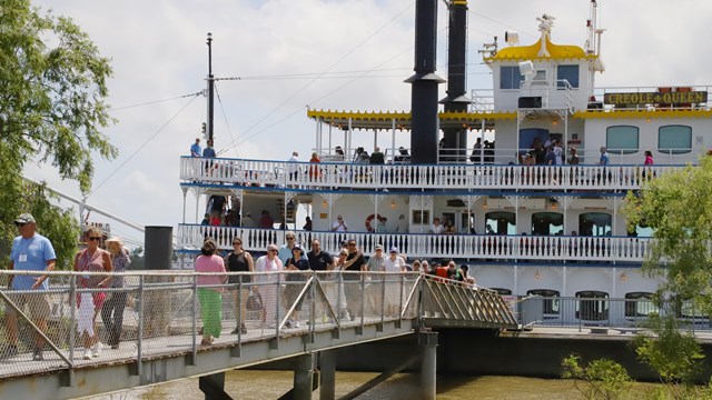 A white paddle boat docked with people walking off the boat onto land.